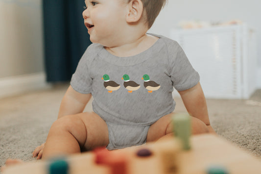 Baby wearing a grey onesie with three mallard ducks across the chest